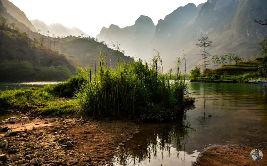 Green grass by the river and mountains in the background.